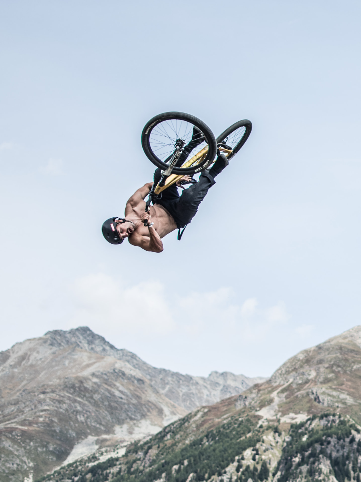 Rider inverted mid-flip against alpine peaks